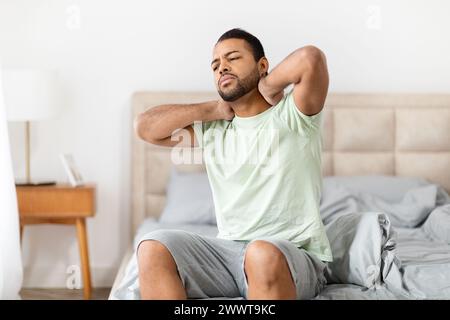 Homme avec mal au cou assis sur le bord du lit Banque D'Images