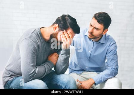 Les membres du groupe réconfortant l'homme accro pleurant à la session de réadaptation Banque D'Images