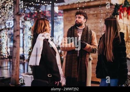 Groupe d'amis heureux partageant des rires lors d'une joyeuse soirée de Noël, entouré de lumières et de décorations festives. Banque D'Images