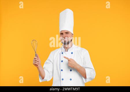 Heureux confiseur professionnel en uniforme pointant au fouet sur fond jaune Banque D'Images