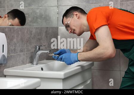 Robinet de réparation de plombier souriant avec clé dans la salle de bain Banque D'Images