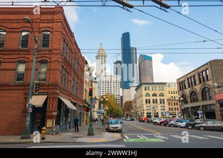 Une rue de ville bordée de bâtiments historiques en briques rouges et en pierre sous des câbles de tramway surplombants, avec des gratte-ciel en arrière-plan, à Seattle, Washington. Banque D'Images