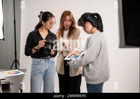 Une photographe professionnelle asiatique discutant avec un directeur artistique et un assistant, se préparant avant un tournage en studio avec Li professionnel Banque D'Images