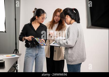 Une photographe professionnelle asiatique discutant avec un directeur artistique et un assistant, se préparant avant un tournage en studio avec Li professionnel Banque D'Images