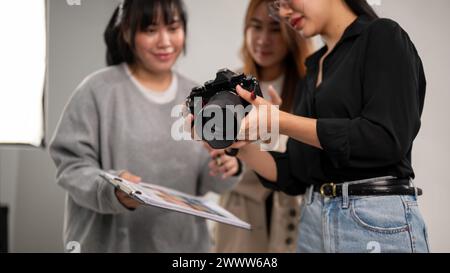 Une photographe asiatique professionnelle montre des images sur son appareil photo à des directeurs artistiques, travaillant avec son équipe dans le studio avec une lumière professionnelle Banque D'Images