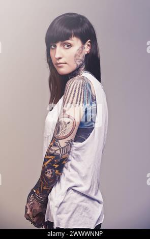 Portrait, culture et femme avec tatouages, confiance et punk rock sur fond gris studio. Visage, personne et modèle avec créativité ou artistique Banque D'Images