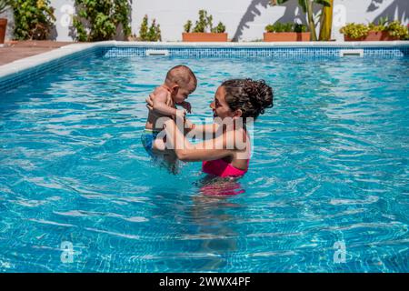 jeune mère tenant son petit bébé dans la piscine, profitant de l'eau ensemble pour la première fois. curiosité, découverte et développement du bébé. se Banque D'Images