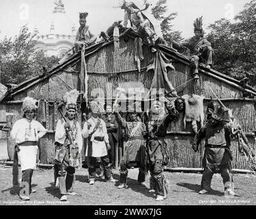 La photographie montre des Amérindiens en tenue traditionnelle et un homme vêtu d'un costume avec un badge d'étoile posé près d'une maison des six Nations long - 1901 Banque D'Images