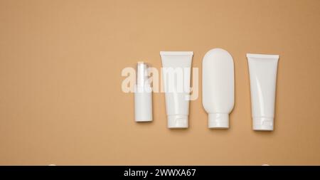 Tubes en plastique blanc, bocaux et récipients pour produits cosmétiques sur fond brun, publicité et marquage des produits Banque D'Images