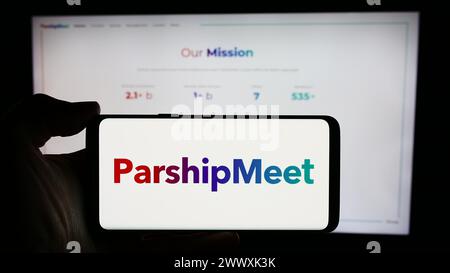Personne tenant le téléphone portable avec le logo de la société allemande de rencontres en ligne ParshipMeet Holding GmbH en face de la page Web de l'entreprise. Concentrez-vous sur l'affichage du téléphone. Banque D'Images