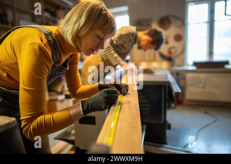 Femme menuisier marquage point sur planche pour scier dans l'atelier de menuiserie avec collègue Banque D'Images