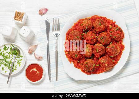 Albondigas, boulettes de viande mexicaines de porc et de bœuf dans une sauce tomate à l'oignon poivron rouge saupoudrée de ciboulette sur plat blanc avec couverts sur bois blanc Banque D'Images