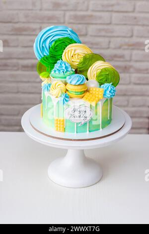 Beau gâteau d'anniversaire vert et jaune coloré sur fond blanc avec sucettes et meringues sur le dessus Banque D'Images