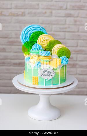 Beau gâteau d'anniversaire vert et jaune coloré sur fond blanc avec sucettes et meringues sur le dessus Banque D'Images