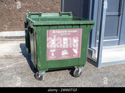 Grand conteneur à ordures en plastique vert ouvert avec des roues dans la rue de la ville. Texte en russe : papier, plastique, verre Banque D'Images