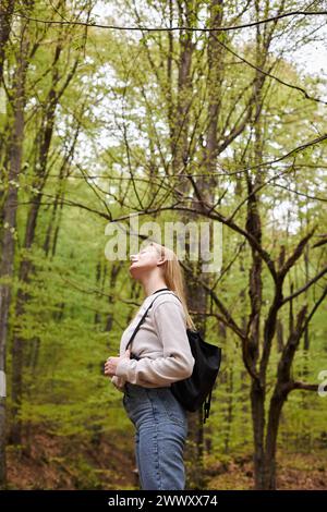 Vue latérale de confortable blonde femme randonneur détendu se reposant avec les yeux fermés dans la vue sur la forêt Banque D'Images