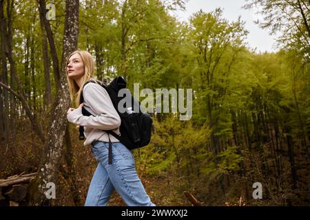 Vue latérale de la femme touriste avec sac à dos marchant au sentier de randonnée dans les bois à la forêt d'automne Banque D'Images