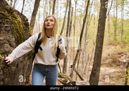 Curieuse femme blonde portant sac à dos sur le voyage de randonnée et marchant près de falaise rocheuse et ruisseau Banque D'Images