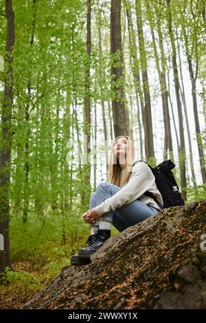 Photo d'une randonneuse embrassant ses jambes portant un pull, un Jean et des bottes de randonnée assis dans la forêt Banque D'Images