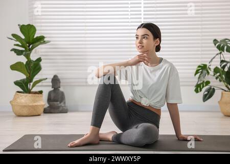Belle fille assise sur le tapis de yoga en studio Banque D'Images