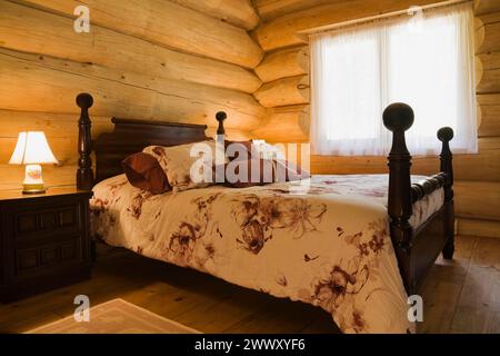 Ancien lit queen size à baldaquin avec couvre-lit à motifs floraux dans la chambre d'amis à l'intérieur de maison de cabane scandinave en bois de pin blanc de l'est artisanale Banque D'Images