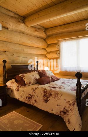 Ancien lit queen size à baldaquin avec couvre-lit à motifs floraux dans la chambre d'amis à l'intérieur de maison de cabane scandinave en bois de pin blanc de l'est artisanale Banque D'Images