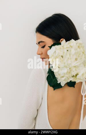 Jeune belle femme avec des fleurs près du visage. Concept de traitement de beauté. Soins de la peau. Jolie femelle avec la santé, peau fraîche du corps. Banque D'Images