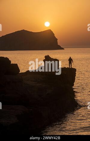 Homme pêchant au coucher du soleil sur la plage de Cala Comte, Joan de sa Talaia, Ibiza, Îles Baléares, Espagne Banque D'Images