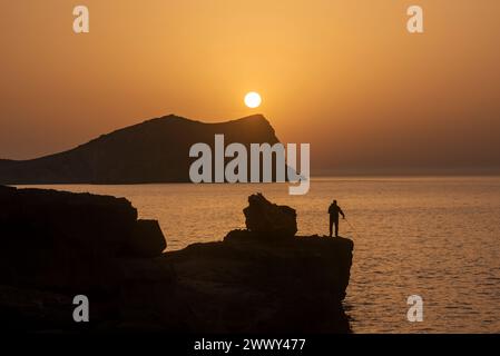 Homme pêchant au coucher du soleil sur la plage de Cala Comte, Joan de sa Talaia, Ibiza, Îles Baléares, Espagne Banque D'Images