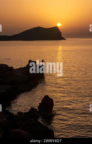 Homme pêchant au coucher du soleil sur la plage de Cala Comte, Joan de sa Talaia, Ibiza, Îles Baléares, Espagne Banque D'Images