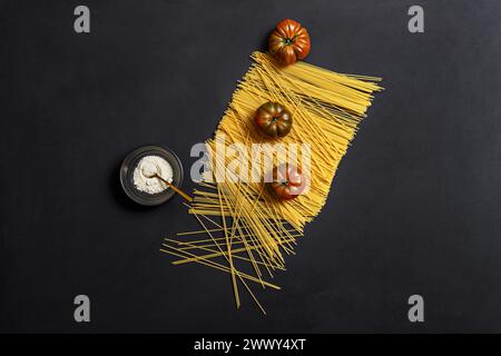 une nature morte simple avec du fromage râpé dans un bol noir, des pâtes spaghetti crues et des tomates mûres Banque D'Images