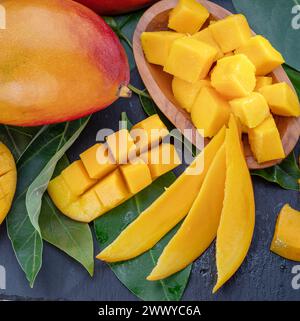 Fruits de mangue mûrs avec tranches et feuilles de mangue sur une table en pierre grise. Beau fond de fruit pour vos projets. Banque D'Images