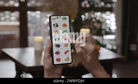 Commander de la nourriture à l'aide d'un smartphone à la maison. Une femme sélectionne des légumes dans une boutique en ligne à l'aide d'une application sur un smartphone. Ameublement de soirée Banque D'Images