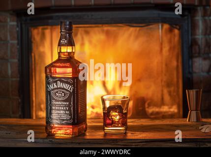 Kiev, Ukraine – 25 mars 2021. Bouteille de whisky Jack Daniels avec un verre de whisky sur une vieille table en bois devant une cheminée en feu, vintage Banque D'Images