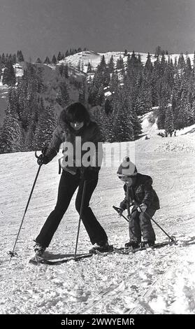 années 1970, historique, alpes, dehors sur une montagne enneigée, une mère montrant à son jeune fils comment skier, Banque D'Images