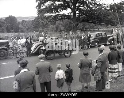 Années 1950, historiques, spectateurs debout au bord de la route regardant une voiture vétéran à toit ouvert prenant part à une course de voitures anciennes, Angleterre, Royaume-Uni. Banque D'Images