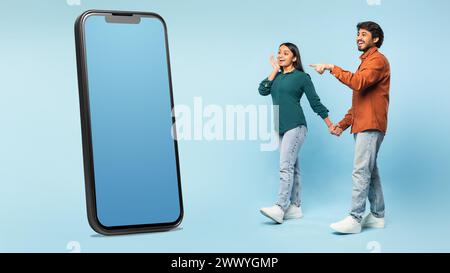 Couple excité du moyen-Orient pointant vers l'écran géant de smartphone, studio Banque D'Images