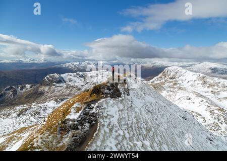 Un marcheur debout sur la crête étroite juste au-delà du sommet rocheux de Meall Garbh avec Beinn nan Eachan sur la droite toute la partie de la crête de Tarmachan Banque D'Images