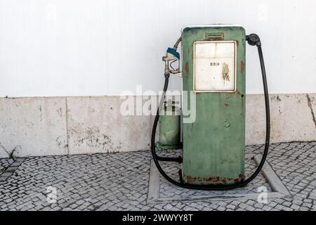 Vieille pompe à essence sur un trottoir au Portugal, avec un mur blanc derrière. Banque D'Images