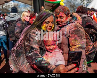 Une famille couverte de poudre colorée est vue prendre un selfie avec le téléphone portable. Des millions de personnes dans le monde entier célèbrent le festival annuel Holi Hangámá, également connu sous le nom de Festival des couleurs, qui signifie célébrer l'arrivée du printemps. À la Haye, où se trouve la plus grande population indienne en Europe, une grande célébration a eu lieu dans le quartier multiculturel du Transvaal, où les participants ont jeté de la poudre aux couleurs vives sur eux-mêmes et les uns sur les autres. Les gens ont célébré cet événement en se promenant dans le quartier en chantant et en dansant dans une procession colorée. Banque D'Images