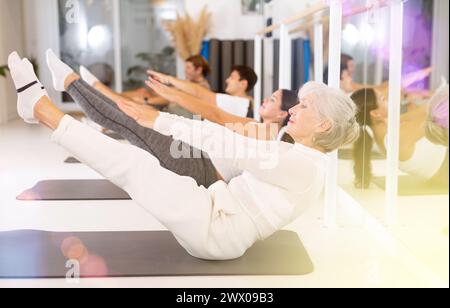 Hommes et femmes sportifs énergiques faisant des exercices sur un tapis de pilates pendant l'entraînement de groupe au gymnase. Banque D'Images