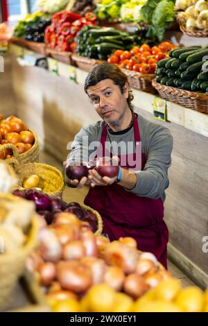 Un travailleur d'épicerie de sexe masculin organise l'oignon rouge et les autres légumes sur le comptoir Banque D'Images