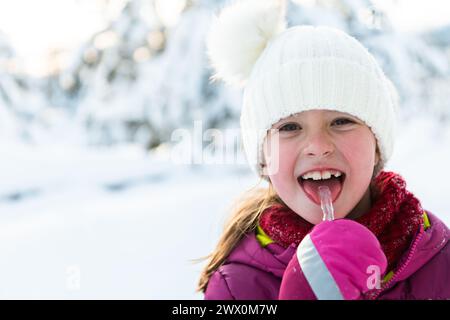 Jolie petite fille tout en mangeant de l'icicle le beau jour d'hiver Banque D'Images