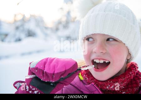 Jolie petite fille tout en mangeant de l'icicle le beau jour d'hiver Banque D'Images