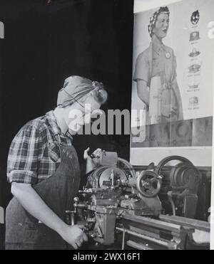 Cette photographie représente une jeune femme employée de l'ordonnance qui a reçu une formation d'usine de munitions par l'Administration nationale de la jeunesse alors qu'elle pose devant une affiche d'employée de l'ordonnance pendant la seconde Guerre mondiale CA. 1939-1943 Banque D'Images