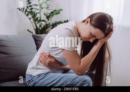 Malsain bouleversé jeune femme souffrant de douleurs menstruelles. Fille triste avec la main pressant le ventre ayant mal à l'estomac douloureux ou crampes de période assis sur Banque D'Images