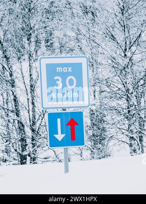 Un panneau de limitation de vitesse bleu et blanc affiche un maximum de 30 kilomètres par heure le long d'une route et la priorité doit être donnée aux véhicules dans la direction opposée Banque D'Images