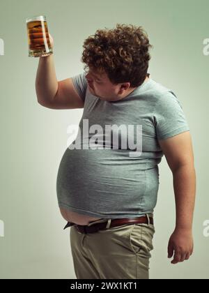 Plus la taille, l'homme et la vérification de la bière pour malsain, habitude et gain de poids dans le studio de fond blanc. Boisson, décision et personne masculine avec boisson dans Banque D'Images