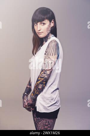 Portrait, culture et femme avec tatouages, rebelle et punk rock sur fond gris studio. Visage, personne et modèle avec créativité ou artistique avec Banque D'Images