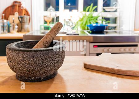 Une planche à découper en bois se trouve sur un comptoir à côté d'un mortier et d'un pilon. La cuisine est bien éclairée et propre, avec une plante en pot en arrière-plan. Concep Banque D'Images